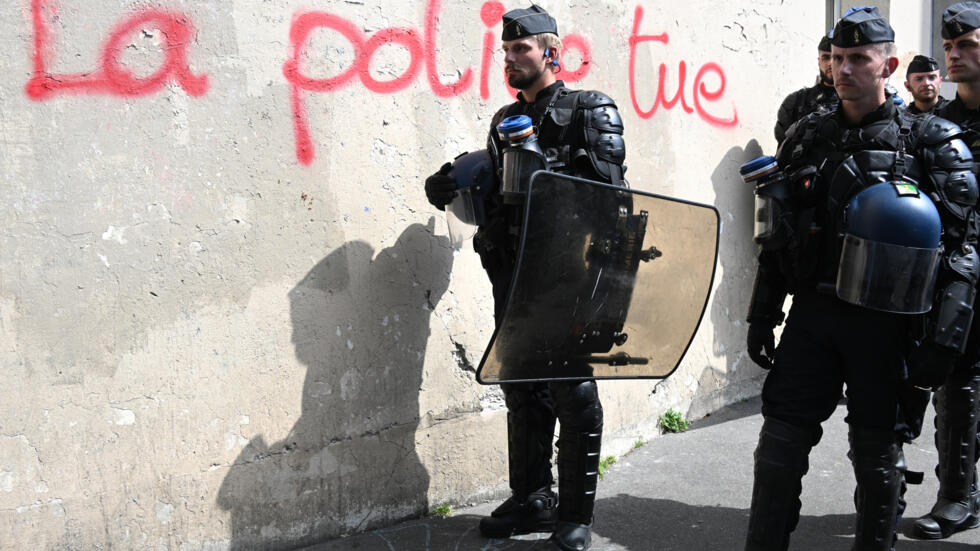 Riot police stand next to graffiti reading "Police kill" during a march in memory of Adama Traoré in Paris on July 8, 2023, seven years after Traoré died shortly after being arrested.